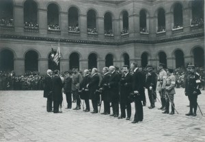 Pershing est situé en face du drapeau américain. Paul Painlevé a placé son chapeau au niveau de sa poitrine et regarde en direction du photographe. Le maréchal Joffre et le général Foch sont placés au second rang, ils sont à peine visibles sur cette photographie. © Paris, musée de l’Armée